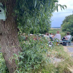 Een groep mensen zittend aan een picknicktafel bij een boom tijdens het Magisch weekend vol mantra's in Fryslân.