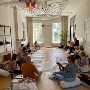 Een groep mensen zittend op yogamatten in een huis.