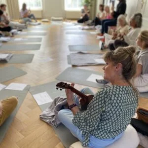 Een groep mensen zittend op de grond die deelneemt aan een UITVERKOCHT Magische Mantra Basis Workshop in Hoorneboeg.