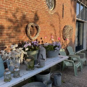 Een Magic Mantra Weekend Fryslân tafel met stoelen en potten met bloemen voor een bakstenen gebouw tijdens het Magic Mantra Weekend.