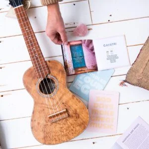 Een persoon die een houten ukelele vasthoudt op een houten tafel.