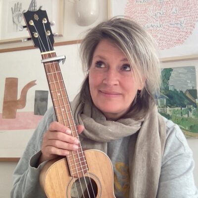 Een vrouw die thuis op een houten ukelele speelt.