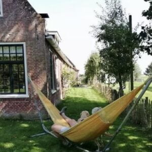 Een persoon die ontspannen in een hangmat voor een huis geniet van het Magic Mantra Weekend Fryslân.