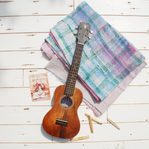 witgechilderd houten paneel met erop een kleed uit India met de kleuren groen roze en blauw en een massief houten. ukelele erop en wat palo santo hout eromheen