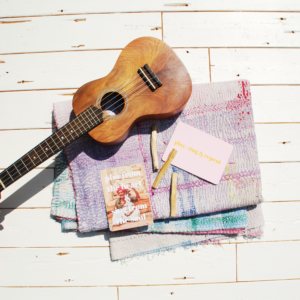 massief houten palo Santo ukelele op witgeschilderd houten bord met kleed uit India met roze en groen